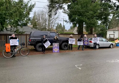 A line of people wearing monkey masks and holding signs stand along a street A line of people wearing monkey masks and holding signs stand along a street